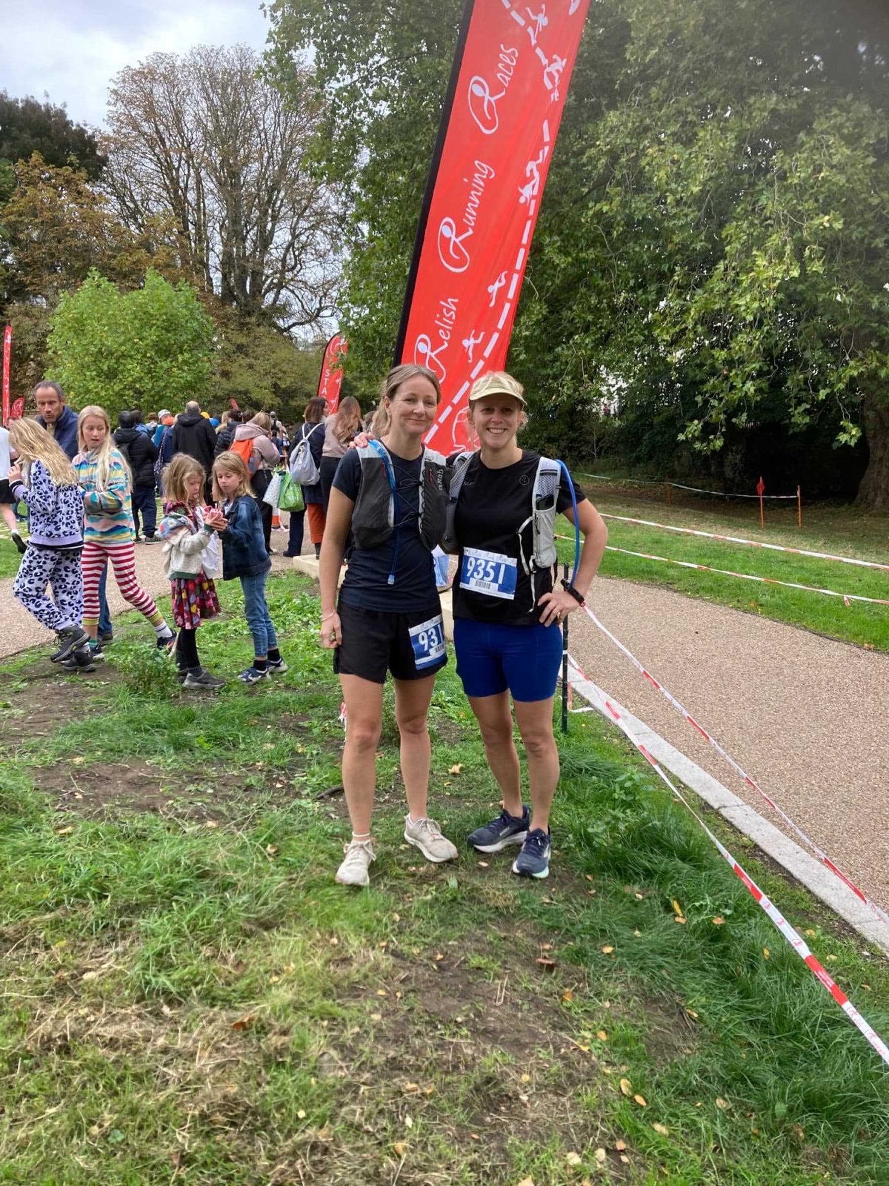 Joy and Helen side by side in running kit after the marathon, in front of a Relish Running Races banner